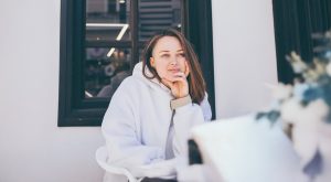 young woman with brown hair in a white hoodie sitting on a porch thinking